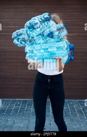 Junge Frau wirft leere gebrauchte Plastikwasserflaschen in den Abfalleimer. Sammeln von Kunststoffabfällen zum Recycling. Konzept der Plastikverschmutzung und auch Stockfoto