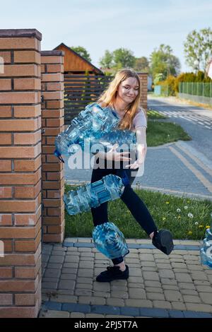 Junge Frau wirft leere gebrauchte Plastikwasserflaschen in den Abfalleimer. Sammeln von Kunststoffabfällen zum Recycling. Konzept der Plastikverschmutzung und auch Stockfoto