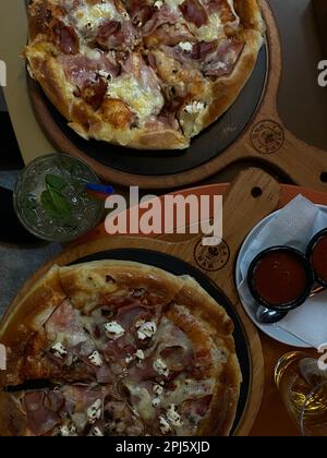 Zwei Pizzen werden auf Holzbrettern mit verschiedenen Belägen und Sauce serviert Stockfoto