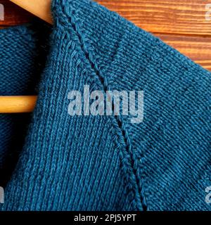 Handgefertigter Pullover. Strickmaterial aus grünem Faden auf braunem Hintergrund.Bereich kopieren Stockfoto