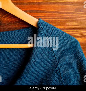 Handgefertigter Pullover. Strickmaterial aus grünem Faden auf braunem Hintergrund.Bereich kopieren Stockfoto