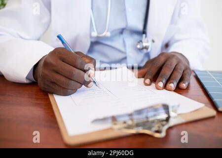 Nahaufnahme von schwarzem Arzt, der die Symptome des Patienten auf dem Klemmbrett am Schreibtisch ausfüllt Stockfoto