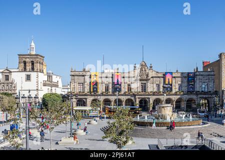 Guadalajara, Jalisco Mexiko. 4. Februar 2023. Stadtbild der Plaza de los Laureles mit Spaziergängern, Bussen, Bäumen, einem Brunnen und dem Palacio Munic Stockfoto