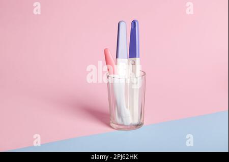 Stillleben. Inkjet-Schwangerschaftstests in Glas, isoliert auf pinkfarbenem Pastellhintergrund. Schnelle Schwangerschaftserkennung. Stockfoto