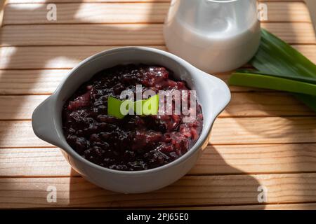 Schwarzer, klebriger Reisbrei mit Kokosmilch-Sauce, serviert in einer weißen Schüssel. Traditionelles indonesisches Dessert Stockfoto