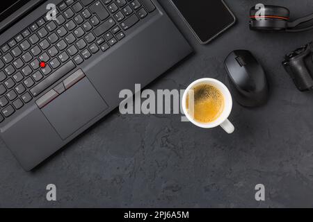 Arbeitsplatz und Büroschreibtisch mit Kaffee, Laptop, Headset und Smarthpone. Flatlay in schwarzem Ton Stockfoto