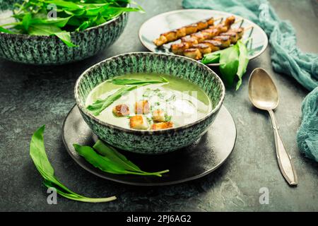 Bärlauch-Suppe oder Ramson-Suppe mit Crouton, Sauerrahm und putenspieß auf grünem Hintergrund Stockfoto