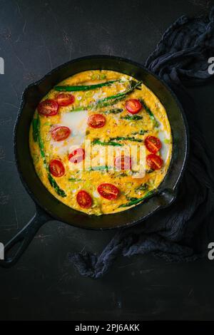 Köstliche Fritatta mit grünem Spargel und Kirschtomaten in der Pfanne Stockfoto