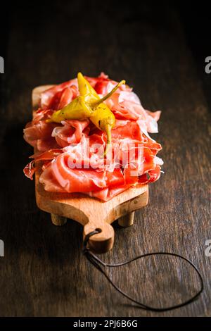 Prosciutto mit gegrillter Paprika – Italienischer Trockenschinken mit gegrillter grüner Paprika auf einem Holztisch Stockfoto