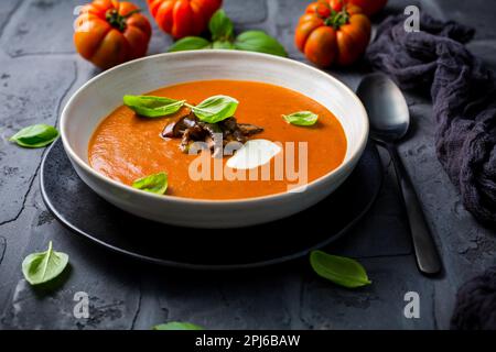 Hausgemachte Tomatensuppe mit gerösteter Aubergine und Basilikum auf dunklem Hintergrund Stockfoto