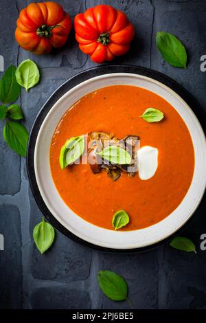 Hausgemachte Tomatensuppe mit gerösteter Aubergine und Basilikum auf dunklem Hintergrund Stockfoto