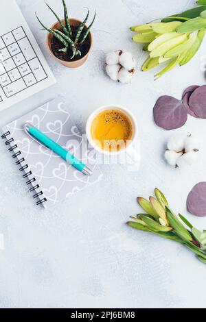 Arbeitsplatz mit einer Tasse Kaffee, leerem Notizbuch, Tastatur, Vorräten und Blumen in hellem Ton Stockfoto