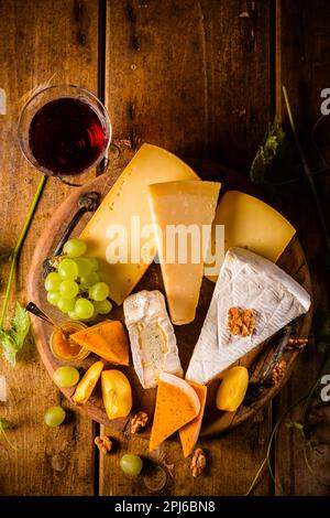 Käseplatte, verschiedene Käsesorten mit einem Glas Rotwein, Trauben auf einem Holztisch Stockfoto