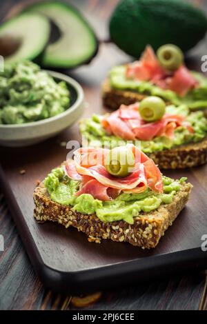 Guacamole Dip or Brotaufstrich mit offenen Sandwiches und Schinken auf Holzküchentisch Stockfoto