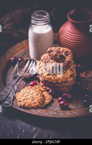 Hausgemachte Haferbrei-Kekse, Preiselbeerkekse und eine Flasche Milch auf einem Holztisch Stockfoto