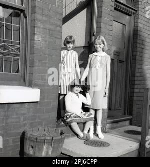 1950er, historisch, drei junge Mädchen mit Hund, die in der Tür ihres viktorianischen Terrassenhauses in einer gepflasterten Straße in Stockport, Manchester, England, standen. Stockfoto