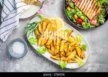 Kartoffelkeile, im Ofen gebraten mit frisch gemischtem Salat und gegrilltem Käse Stockfoto