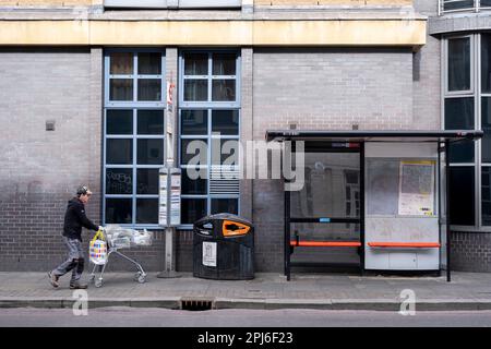 Mann schiebt einen Einkaufswagen an einer Bushaltestelle in Hoxton am 6. März 2023 in London, Großbritannien vorbei. Stockfoto