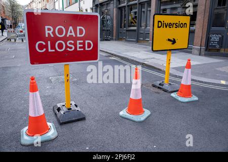 Am 27. März 2023 in London, Vereinigtes Königreich, treten Verkehrsschilder und Verkehrskegel mit vorbeifahrenden Personen in Kontakt. Stockfoto