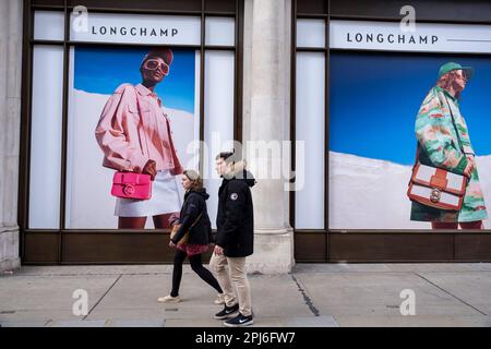 Große Werbebilder für den Modehändler Longchamp am 30. März 2023 in London, Vereinigtes Königreich. Vorbeifahrende Menschen interagieren mit den Figuren auf diesen Fotos, als ob sie im Vergleich klein wären. Longchamp ist ein französisches Lederwarenunternehmen, das 1948 in Paris von Jean Cassegrain gegründet wurde. Diese Gegend der Hauptstadt ist bekannt für ihre exklusiven Geschäfte, deren Vrands sich an die Reichen und Reichen richten. Stockfoto