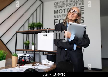 Porträt einer lächelnden erwachsenen Freiberuflerin mit grauen Haaren mit einem Laptop im Haus Stockfoto