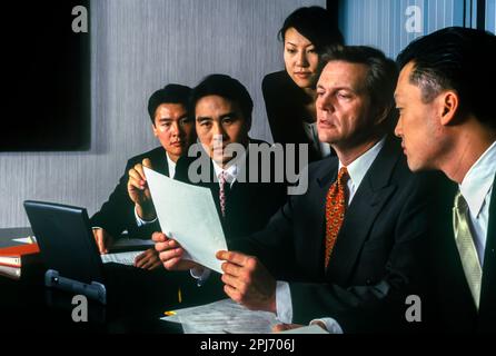 1996 HISTORISCHE ASIATISCHE BÜROANGESTELLTE, DIE PAPIERDOKUMENTE LESEN, WÄHREND SIE SICH AM TISCH TREFFEN Stockfoto