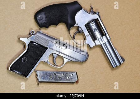 Die kompakte Revolverpistole, die M60-Pistole aus Edelstahl mit j-Rahmen und die kompakte PPKs mit halbautomatischer Pistole sind auf braunem Hintergrund isoliert. Stockfoto