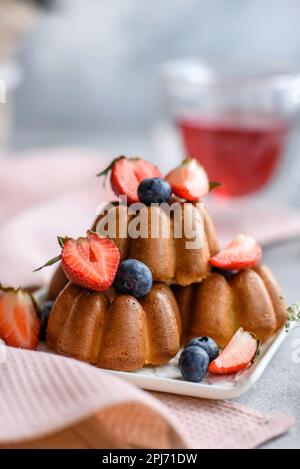 Köstliche Cupcakes oder Muffins mit Rosinen und Nüssen, Erdbeeren und Heidelbeeren auf einem Keramikteller auf einem Tisch aus strukturiertem Beton Stockfoto