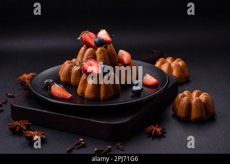 Köstliche Cupcakes oder Muffins mit Rosinen und Nüssen, Erdbeeren und Heidelbeeren auf einem Keramikteller auf einem Tisch aus strukturiertem Beton Stockfoto