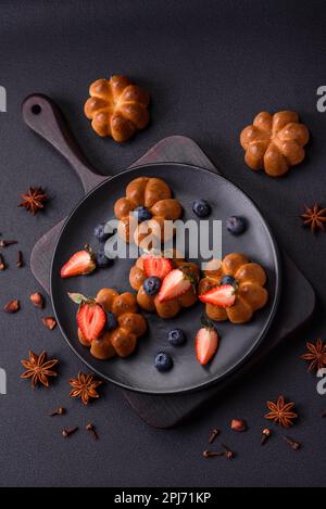 Köstliche Cupcakes oder Muffins mit Rosinen und Nüssen, Erdbeeren und Heidelbeeren auf einem Keramikteller auf einem Tisch aus strukturiertem Beton Stockfoto