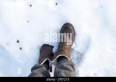 Braune Damenstiefel im Schnee an einem sonnigen Tag Stockfoto