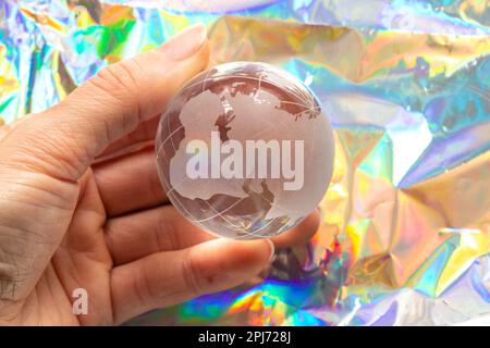 Die Glaskugel des Planeten in der Hand hält ein Mädchen auf einem farbigen Hintergrund Nahaufnahme Stockfoto