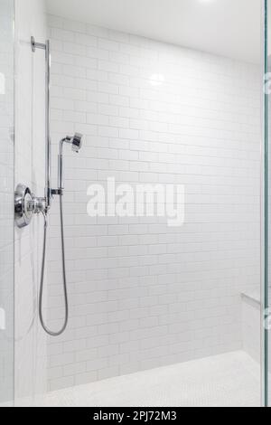 Eine große begehbare Dusche mit weißen Wänden mit Subway-Fliesen, weißem rundem Fliesenboden und einem Chromhahn. Stockfoto