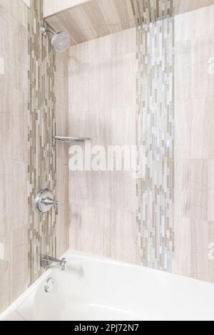 Eine Dusche mit großen braunen Fliesen und kleinen Subway-Fliesen-Akzenten, Chrom-Duschkopf und eine weiße Badewanne. Stockfoto