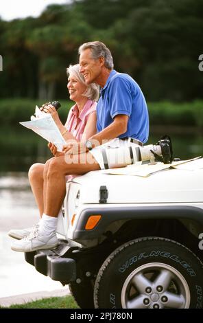 Ein pensioniertes Paar, das auf der Haube des Jeeps sitzt und während des Urlaubs auf eine Karte schaut Stockfoto