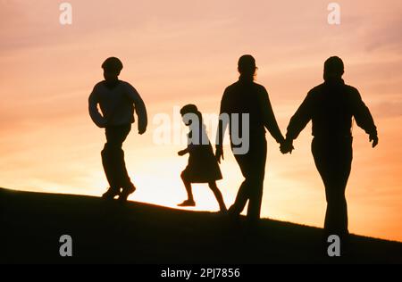 Silhouette einer vierköpfigen Familie, die bei Sonnenuntergang auf einem Hügel spaziert Stockfoto