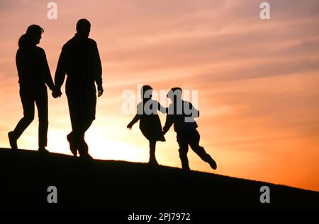 Die Silhouette einer Familie, die bei Sonnenuntergang auf einem Hügel spaziert Stockfoto