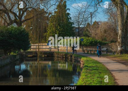 Menschen gehen am River Eye in Lower Slaughter in Cotswolds England an sonnigen Tagen entlang Stockfoto