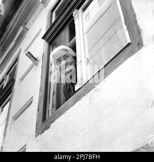 Sibiu County, Rumänien, ca. 1976. Ältere Frau, die aus dem Fenster ihres Hauses schaut. Stockfoto