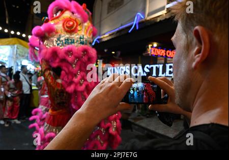 Bangkok, Thailand. 30. März 2023. Ein Tourist fotografiert chinesische Löwentänzer, die sich auf der Straße vortäuschen. Bangkoks berüchtigtes Rotlicht-Unterhaltungsviertel Patpong wurde seit der COVID-19-Pandemie wieder eröffnet. Es ist wieder ein Street Food Nachtmarkt mit nur wenigen Go Go Go Bars, 2 Straßen bieten auch Souvenirs, Kleidung und Schmuck. Seit der Legalisierung von Marihuana am 9. Juni wurden auch Marihuana-Verkaufsstellen in der Region eröffnet. (Foto: Paul Lakatos/SOPA Images/Sipa USA) Guthaben: SIPA USA/Alamy Live News Stockfoto