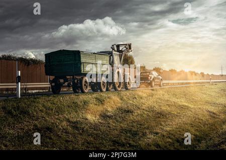 Traktor hinter einem Auto-Lkw auf einer Landstraße in der Sonne mit Sonnenstrahlen und düsterer Sisko Stockfoto
