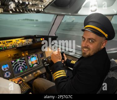Kaukasischer bärtiger Mann, der beim Fahren eines Flugsimulators lächelt. Der Pilot im Cockpit zeigt Daumen nach oben. Stockfoto