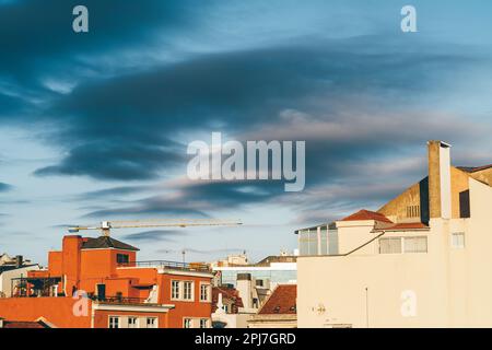 Ein blauer Himmel mit gepunkteten dunklen Wolken und ein großes helles orangefarbenes Haus heben sich von dem anderen in der Szene ab und erzeugen einen lebendigen Kontrast. Die helle Farbe Stockfoto