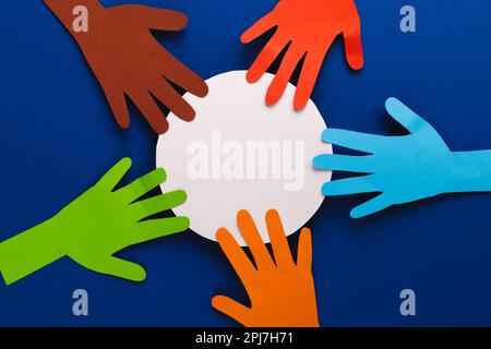 Aus mehrfarbigen Händen ausgeschnittenes Papier und weißer Kreis mit Kopierbereich auf blauem Hintergrund Stockfoto