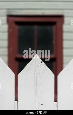 Fenster mit lackiertem Holzrahmen und weißem Lattenzaun im Vordergrund Stockfoto