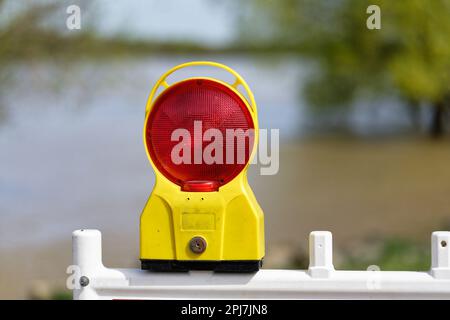 Warnlampe auf einem Absperrgitter vor Hochwasser auf einem Fluss mit verschwommenem Hintergrund Stockfoto