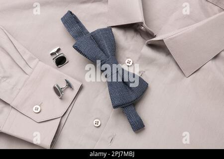 Elegante blaue Fliege und Manschettenknöpfe auf beigefarbenem Hemd, Draufsicht Stockfoto