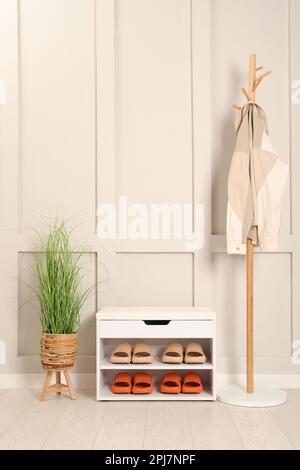 Elegante Aufbewahrungsbank mit verschiedenen Paar Gummipantoffeln und wunderschönen Zimmerpflanzen in der Nähe der weißen Wand im Flur Stockfoto