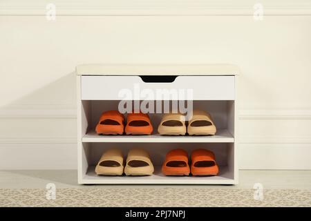 Eleganter Aufbewahrungsschrank mit verschiedenen Paar Gummipantoffeln in der Nähe der weißen Wand im Flur Stockfoto