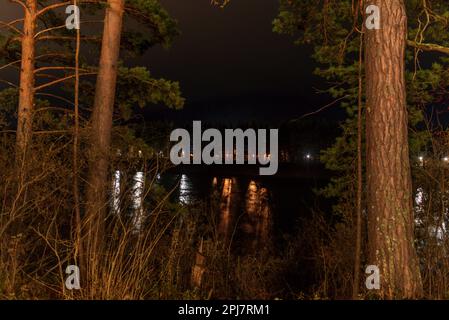 Licht am anderen Ufer des Flusses Katun von Raststätten bei Nacht zwischen den Bäumen in Altai. Stockfoto